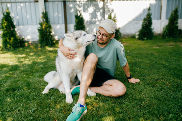 友谊一个可爱的男人和一只狗在草地上摆姿势人微笑哈士奇