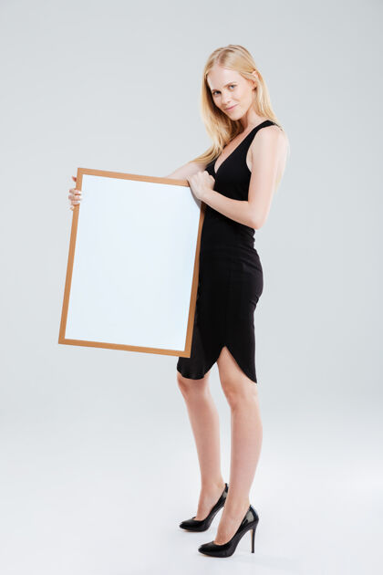 板一位面带微笑的美女手持白板 看着隔离在白色背景上的相机的全长肖像商业女性显示漂亮