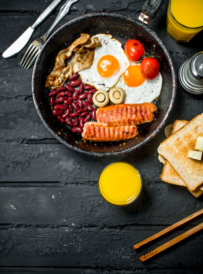 桌子传统的英式早餐 在黑色乡村餐桌上放着橙汁木头平底锅全麦