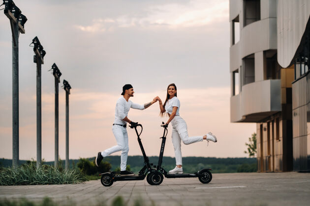 驾驶一个女孩和一个男孩骑着电动滑板车在城市里走来走去 一对恋人骑着滑板车科技夫妻积极