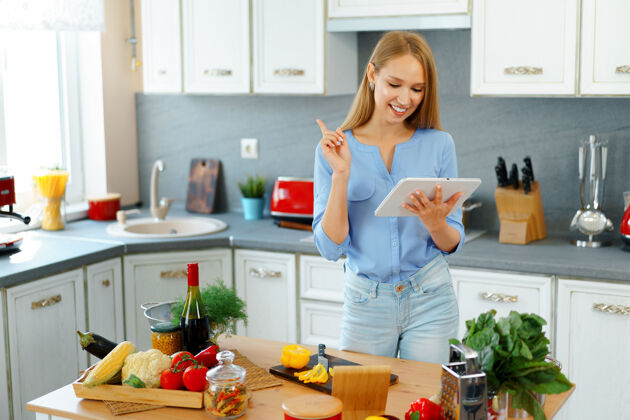 互联网年轻漂亮的白种女人在厨房做饭和使用她的数字平板电脑健康食物现代