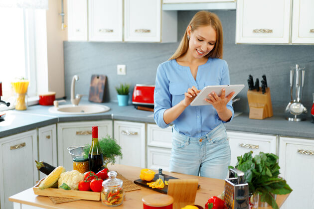 食谱年轻漂亮的白种女人在厨房做饭和使用她的数字平板电脑蔬菜烹饪食物