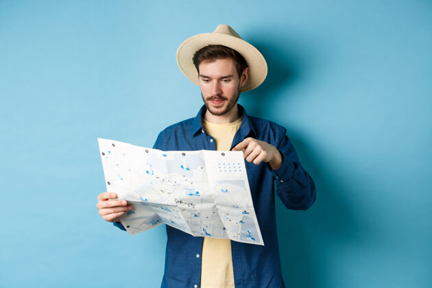 帽子帅哥选择去的地方 度假的时候指着地图 暑假的时候旅游 戴着草帽和衬衫 蓝色的背景站帅气休闲