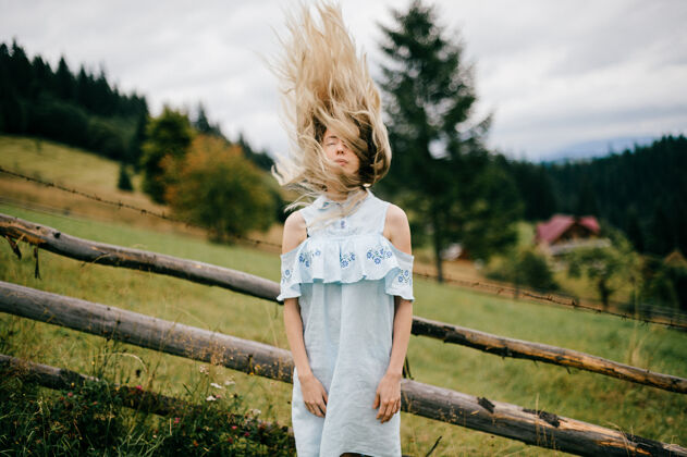 服饰年轻漂亮的金发碧眼的女孩 穿着蓝色的裙子 满头飞舞的头发 在乡村的篱笆边摆姿势女人木头人