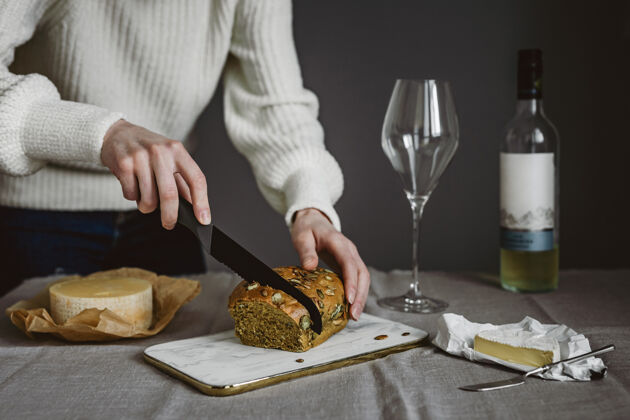 场景一个切面包的女人 几种奶酪 一个酒杯和一瓶白葡萄酒横向生活方式照片手食物水平