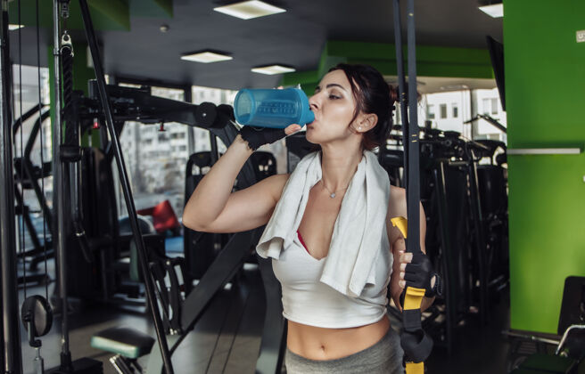活动疲惫的年轻健美女子在健身房喝水室内瓶子训练