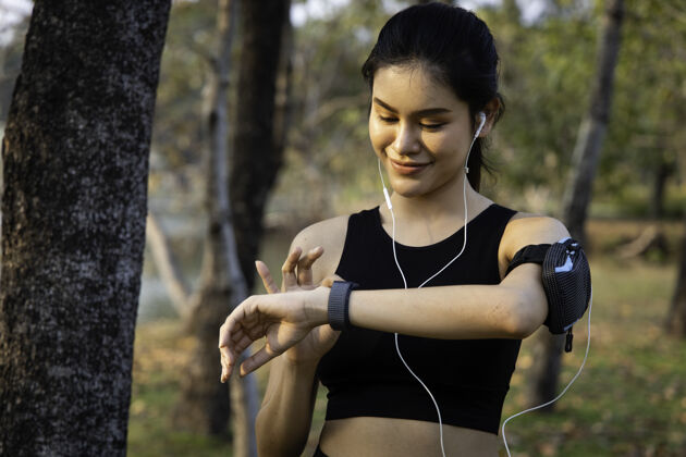 人一位亚洲女子跑步者用智能手表监视她的表现运动员在跑步前在smartwatch上设置健身应用程序智能手表健康健康