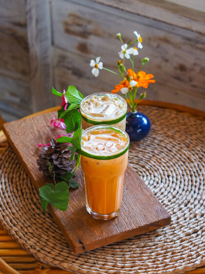 稻草在咖啡厅的木制古董桌上 近距离地放上一杯泰国奶茶和带有花卉装饰的冷咖啡茶水冷