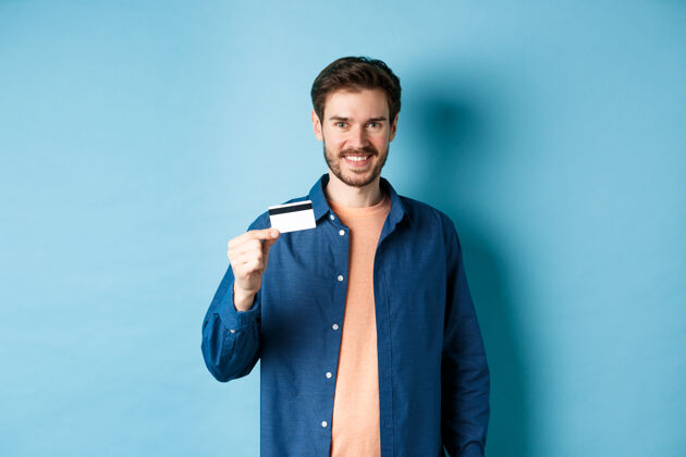 信用卡帅哥笑容可掬地拿着塑料信用卡 站在蓝色的背景上 看上去很满意买家情感展台