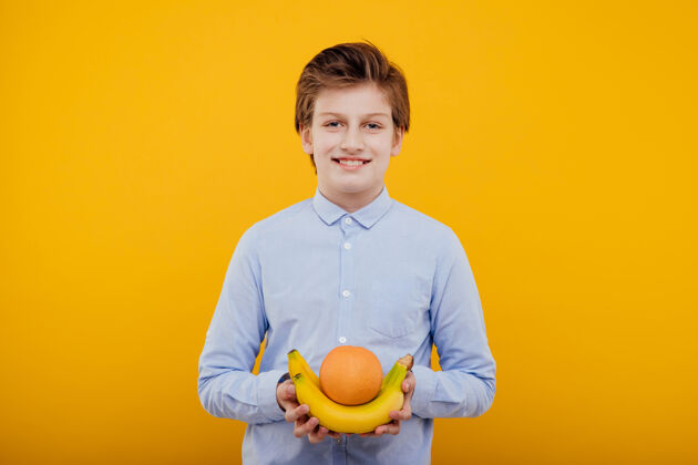 孩子可爱的未成年男孩 手拿水果 穿着蓝色衬衫 隔离在黄色的墙上休闲英俊快乐