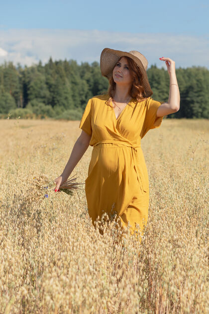 农场在一个阳光明媚的夏日 一位年轻漂亮的孕妇穿着黄色的裙子 戴着黄色的帽子 走过一片麦田肥料自然收获