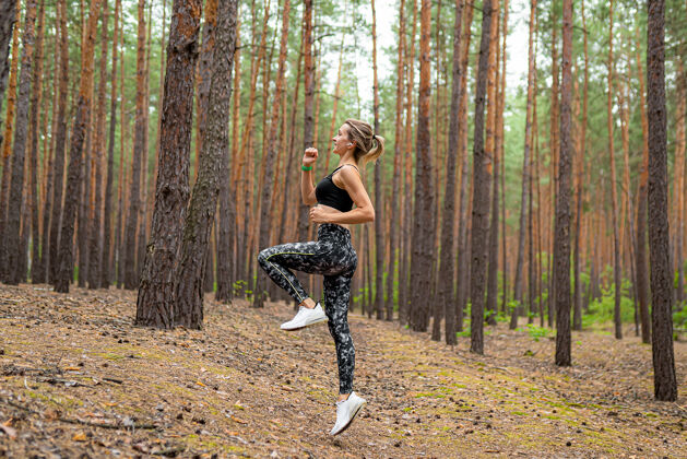 运动一个穿着运动服的女人在松树公园跳跃的侧视图健康身体动机