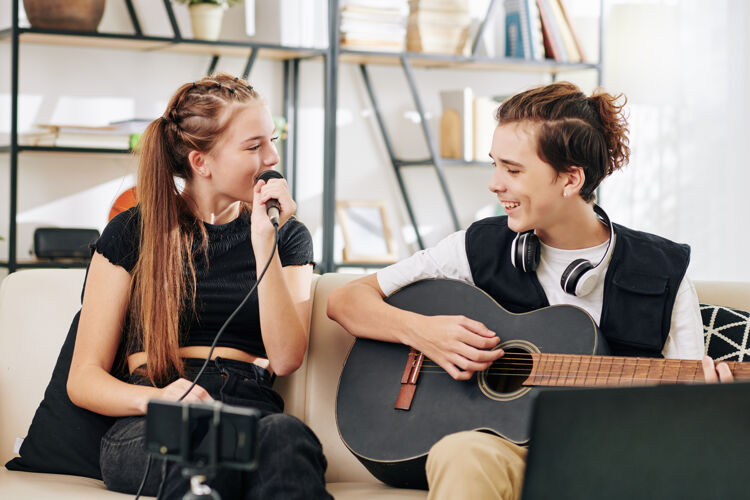 交谈十几岁的男孩弹吉他时 他的妹妹在麦克风里唱歌时 在智能手机上录制视频科技快乐娱乐