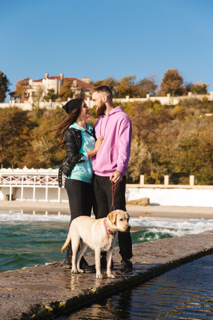 高加索迷人的年轻夫妇带着他们的狗在海滩散步风格友谊配对