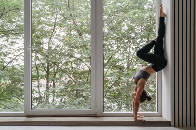 热身迷人的瑜伽女孩在日光下靠着大窗户站在墙上室内课程锻炼
