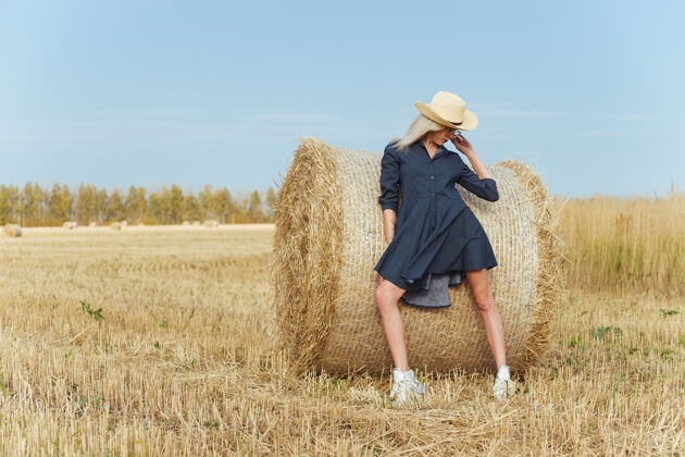 姿势一位年轻漂亮的女村民在一捆干草旁摆出一身衣服田野美丽帽子