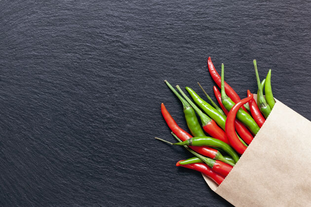 辣椒新鲜辛辣的红 绿辣椒装在一个牛皮纸袋子里 放在一块石板上 各种颜色的辣椒和辣椒从上面呈深色背景顶视图 复制空间墨西哥烹饪素食