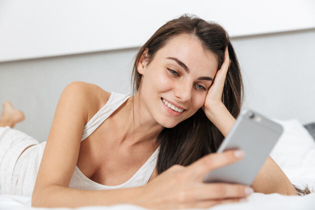 休息美丽的年轻女子在家里的床上放松 用手机吸引力漂亮手机