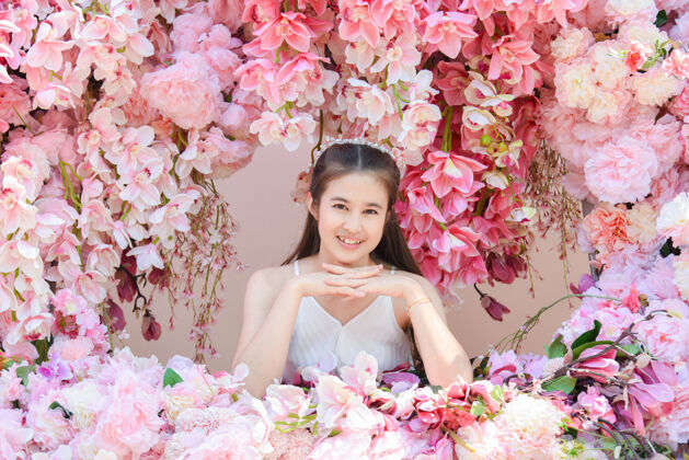 年轻美丽的亚洲女人穿着白色的裙子坐在美丽的粉红色的花快乐漂亮肖像