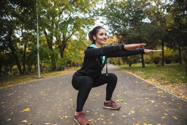 物理微笑的年轻健身女孩在公园里做运动 蹲着身体白种人减肥