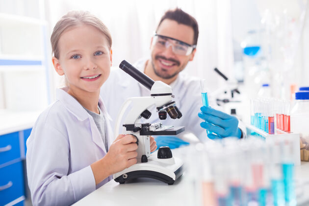 智能令人兴奋的观察快乐积极的女孩 一边笑着 一边触摸显微镜 一边盯着相机健康尼斯实验室