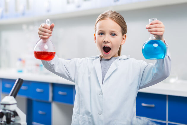 科学五彩液体惊讶小女孩惊讶地举起灯泡 一边灌满不同的液体 一边张嘴玻璃器皿化学人