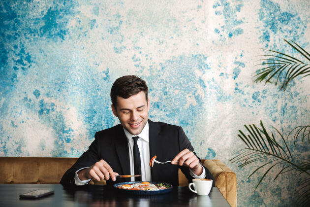 咖啡馆一个开朗英俊的年轻商人坐在咖啡馆里吃早餐或晚餐的形象成年人年轻人饮食