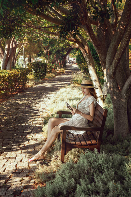 女孩一个手里拿着书的女孩坐在一张长椅上 树荫如画生活方式坐着衣服时尚