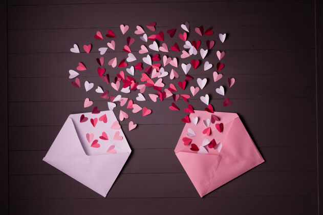 平铺红色 白色和粉红色的纸心在打开的粉红色和白色的灰色木制信封形状节日信