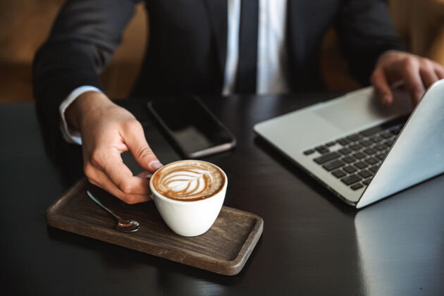 西装一张年轻帅气的商人坐在咖啡馆里用笔记本电脑喝咖啡的剪贴照片工人咖啡英俊