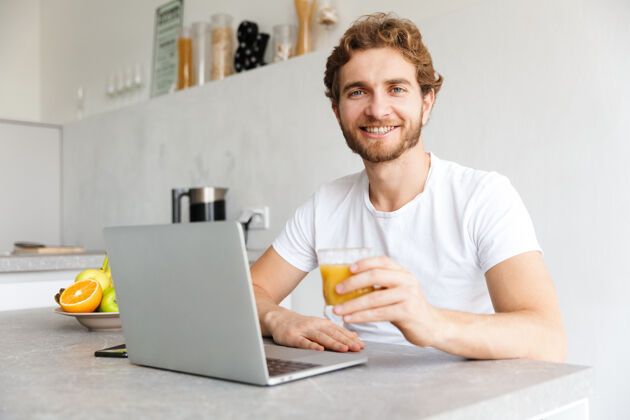 柔软快乐的小胡子男人在家里的桌子上用笔记本电脑成人果汁水果
