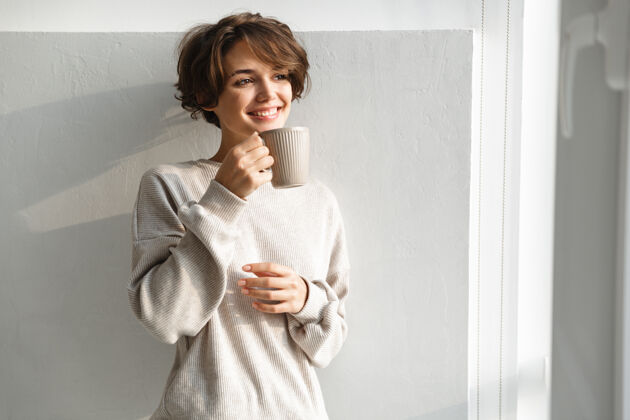 热微笑的年轻女子早上在厨房喝茶温暖年轻茶