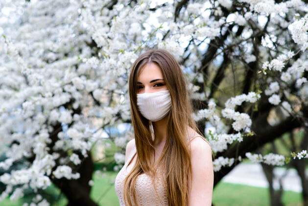 女性在樱花盛开的樱花树下 一个穿着白色上衣 戴着冠状病毒花朵面具的温柔女孩的特写镜头流行病人检疫