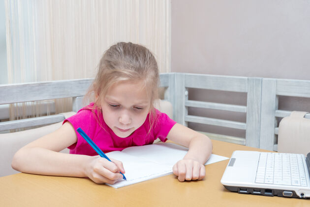 学生一个小女孩坐在桌边 拿着笔记本电脑 在笔记本上写作业学校小学生课堂