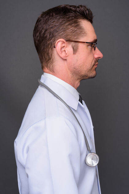 成人长着胡子的帅哥医生戴着眼镜靠着灰墙眼镜医生实验室