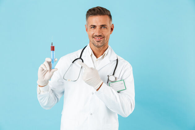 注射自信的男医生穿着制服 孤立地站在蓝色的墙上 展示着一个装有红色液体的注射器职业医生白种人