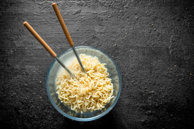 烹饪用筷子夹碗里的热方便面放在黑色的乡村桌子上美味亚洲菜顶部