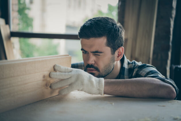 建筑特写专注自信严肃的男人闭着一只眼测量两块木板之间的距离工匠木板男