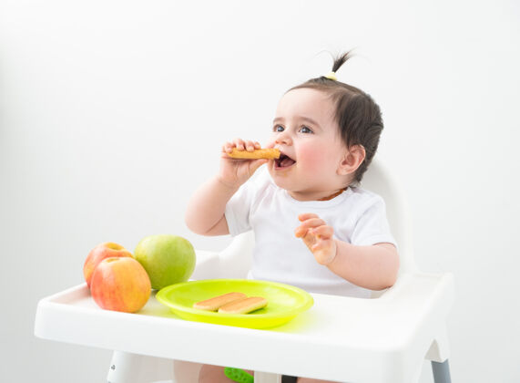 婴儿坐在婴儿椅上吃苹果和饼干的女婴父母健康营养