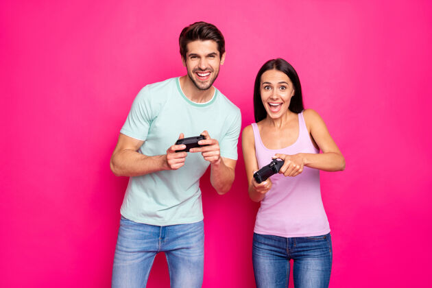 头发搞笑男女情侣周末一起玩电子游戏的资料照片最好穿休闲装隔离粉色背景时髦游戏板休闲