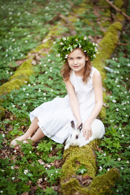 可爱穿着白色连衣裙的漂亮小女孩 在春天的树林里和白兔在一起护理兔子户外