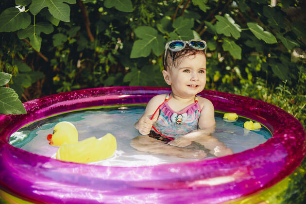 人欢快的宝宝在小游泳池里享受着一天 手里拿着太阳镜 五颜六色的画像欢呼孩子宝宝