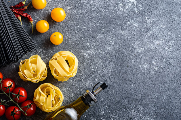 表面意大利晚餐的配料：意大利面 黑意大利面 意大利面 西红柿 橄榄油 红辣椒 灰色背景 空白食物目录烹饪