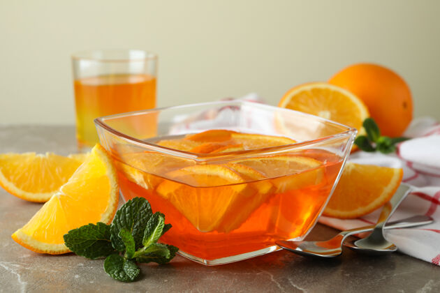 美食甜点的概念是在灰色的桌子上放一碗橘子果冻和橘子片美食明胶冷