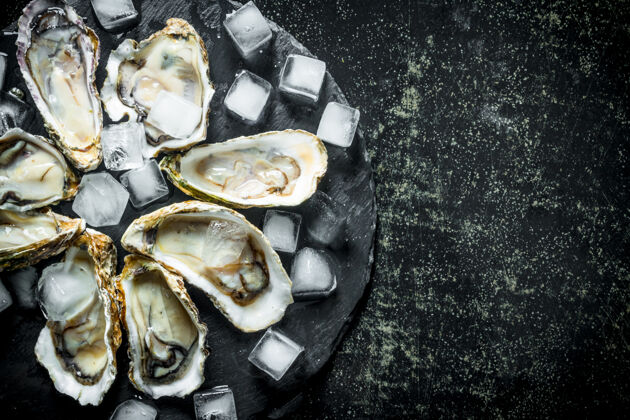 可食用新鲜的牡蛎和冰块放在黑木桌上的圆石板上美味豪华食物