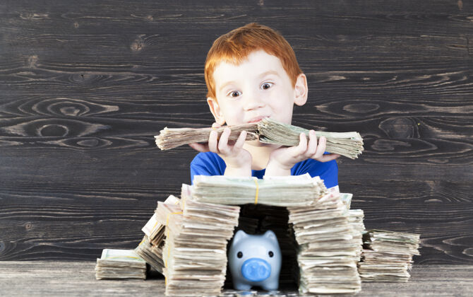 室内红发男孩用硬币为他的蓝色小猪存钱罐盖了一个装满纸钱的房子 特写镜头是一个拿着包裹好的钞票的孩子后代小欢呼