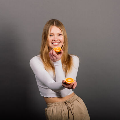 女人微笑的女人在工作室里吃橘子 半个水果 金色的长发切片自然时尚模特