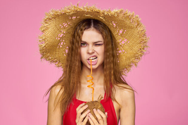 成人戴着草帽的椰子鸡尾酒的女人异国情调的度假夏日粉色的墙壁黑发时尚异国水果