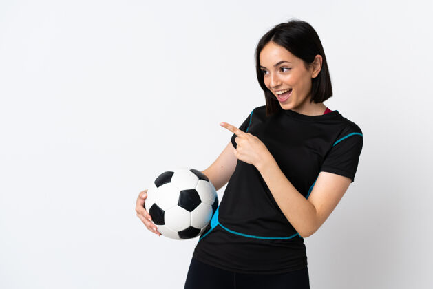 年轻一个年轻的足球运动员 一个被隔离在白墙上的女人 手指着旁边 展示着一个产品产品比赛笑