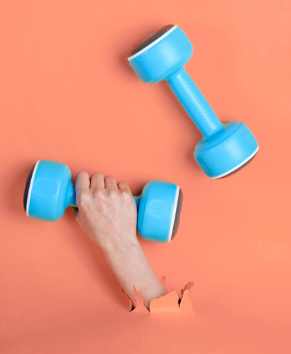 设备女手拿着蓝色塑料哑铃穿过撕破的粉色纸简约运动理念锻炼能量质量